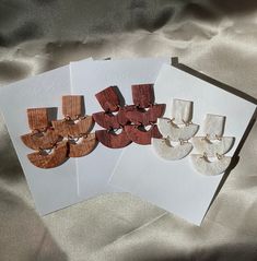 four pairs of wooden earrings on top of white cards with envelopes and silver foil