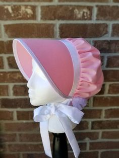 a pink and white hat on top of a mannequin's head in front of a brick wall