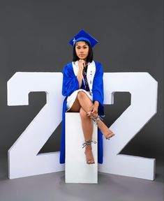 a woman in a graduation cap and gown sitting on top of a large white sign