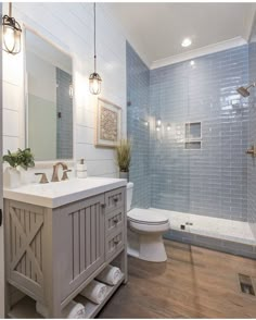 a white toilet sitting next to a walk in shower under a bathroom mirror and light fixture