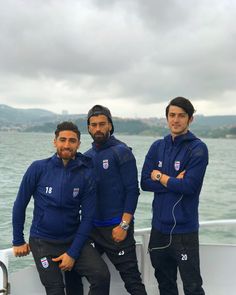 three men on a boat posing for the camera while wearing blue jackets and black pants