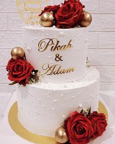 a three tiered wedding cake with red roses on the side and gold decorations at the top