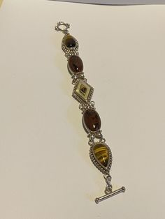 "This is a unique and gorgeous, vintage Whitney Kelly multi stone and sterling silver bracelet that features natural Tiger's Eye, Mother of Pearl and Mahogany Obsidian stones. The bracelet is 7 3/4 inches. The stonework is stunning on the bracelet. The stones are geometric with the Tiger's Eye a teardrop cut, the Mahogany Obsidian an oval cut and the Mother of Pearl a diamond cut. The center Mother of Pearl also has a diamond-cut Tiger's Eye inlaid in its center - so pretty. Even the sterling si Handmade Sterling Silver Brown Bracelet, Handmade Brown Sterling Silver Bracelets, Vintage Brown Bracelet With Natural Stones, Vintage Brown Bracelets With Natural Stones, Vintage Sterling Silver Bracelet With Natural Stones, Vintage Sterling Silver Bracelets With Natural Stones, Vintage Sterling Silver Cabochon Bracelets, Vintage Sterling Silver Bracelets With Cabochon, Collectible Silver Bracelets With Natural Stones