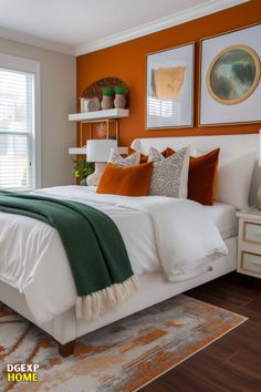 a bedroom with an orange accent wall, white bedding and green throw blanket on the headboard