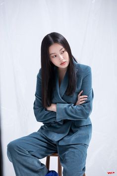 a woman sitting on top of a wooden stool wearing a blue suit and matching shoes