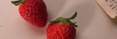 two red strawberries sitting on top of a white table next to a piece of paper