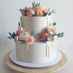 a three tiered white cake with flowers on top and dripping icing down the side