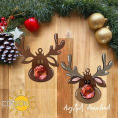 two metal reindeer head ornaments sitting on top of a wooden table next to pine cones