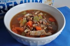 a bowl of soup with beans and carrots next to a carton of milk