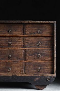 an old wooden dresser with many drawers and knobs on the bottom drawer, against a black background