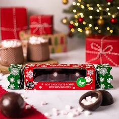 a box of hot chocolates with marshmallows on the table next to christmas presents