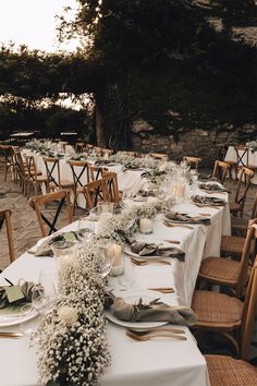 a long table is set up with white flowers and greenery for an outdoor wedding reception