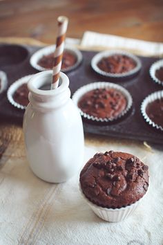 chocolate muffins sitting on top of a table next to a bottle of milk