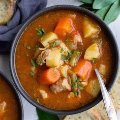 two bowls of soup with bread and vegetables on the side, next to each other