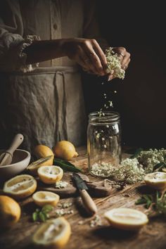 someone sprinkling flowers into a jar filled with lemons on a wooden table