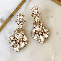 two pairs of earrings sitting on top of a marble table next to a gold ruler