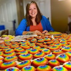 a woman sitting at a table covered in rainbow colored donuts and reading a book