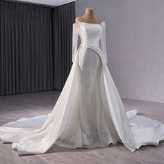 a white wedding dress with long sleeves on display in front of a curtained window