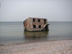 an old concrete structure sitting in the middle of the ocean on top of a sandy beach