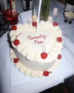 a heart shaped cake with cherries and candles on a table next to wine bottles