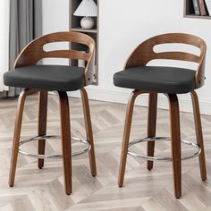 two wooden barstools with black upholstered seats in front of a bookcase