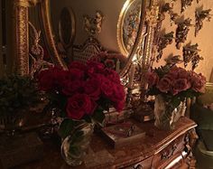 red roses sit in vases on an antique dresser next to a gold framed mirror