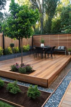 a wooden deck in the middle of a garden with trees and plants on it, surrounded by gravel