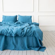 a bed with blue sheets and pillows on top of it in front of a white wall