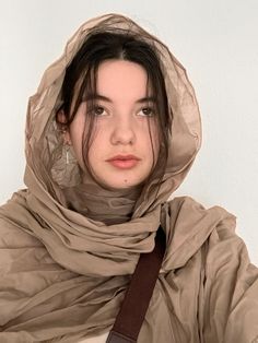 a young woman wearing a brown scarf and hood over her head is looking at the camera