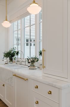 a white kitchen with marble counter tops and gold faucets on the windowsill