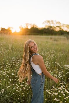 a woman is standing in the middle of a field with daisies and smiling at the camera