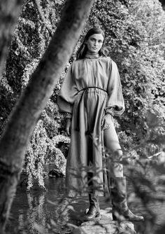 a woman standing in the woods wearing a long dress