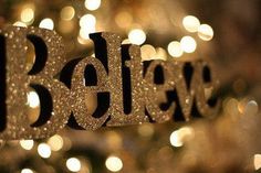 the word believe spelled in gold glitter on a black and white background with boket lights