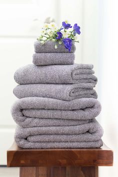 a stack of folded towels sitting on top of a wooden table next to a vase with flowers