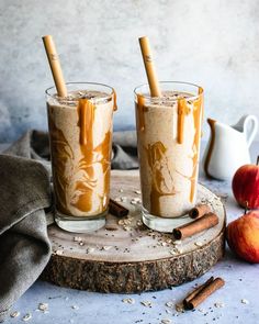 two glasses filled with caramel apple cider latte on top of a wooden board