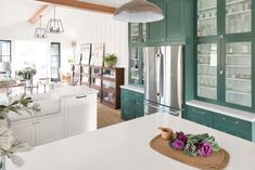 a kitchen with green cabinets and white counter tops, along with a wooden cutting board that has flowers on it