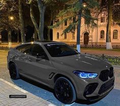 a grey bmw suv parked on the side of a road at night with trees in the background