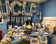 a woman sitting on top of a bed surrounded by foil balloons and other items that spell out her name