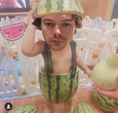 a young boy wearing a watermelon hat and holding two pieces of fruit in front of him