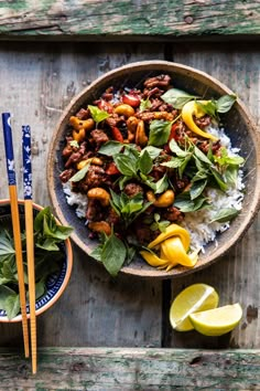 a bowl filled with meat and vegetables next to chopsticks on a wooden table