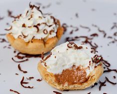 two desserts on a white plate with chocolate sauce and whipped cream