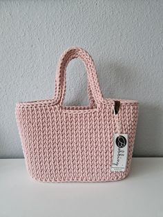 a pink knitted bag sitting on top of a white table next to a wall