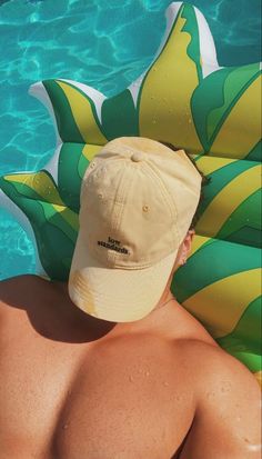 a man wearing a hat sitting next to a swimming pool with inflatable rafts