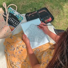 a woman is sitting on the grass and drawing with her crayon pencils