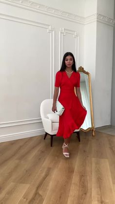 a woman standing in front of a mirror wearing a red dress and holding a white purse