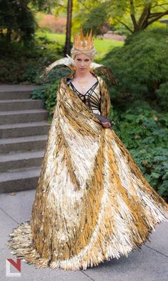 a woman in a gold dress and crown is standing on some steps with her hands behind her back