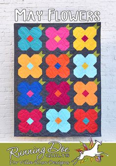 a quilted wall hanging on the side of a white brick building with text overlay that reads, may flowers running bee quilts