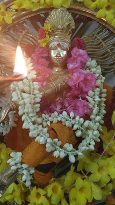 a statue with flowers around it and a lit candle in the background, surrounded by yellow and pink flowers