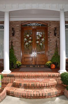 the front entrance to a brick house with two wreaths on each door and steps leading up to it