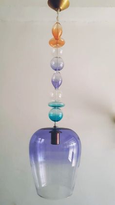 a multicolored glass vase hanging from a metal hook on a white wall in a room